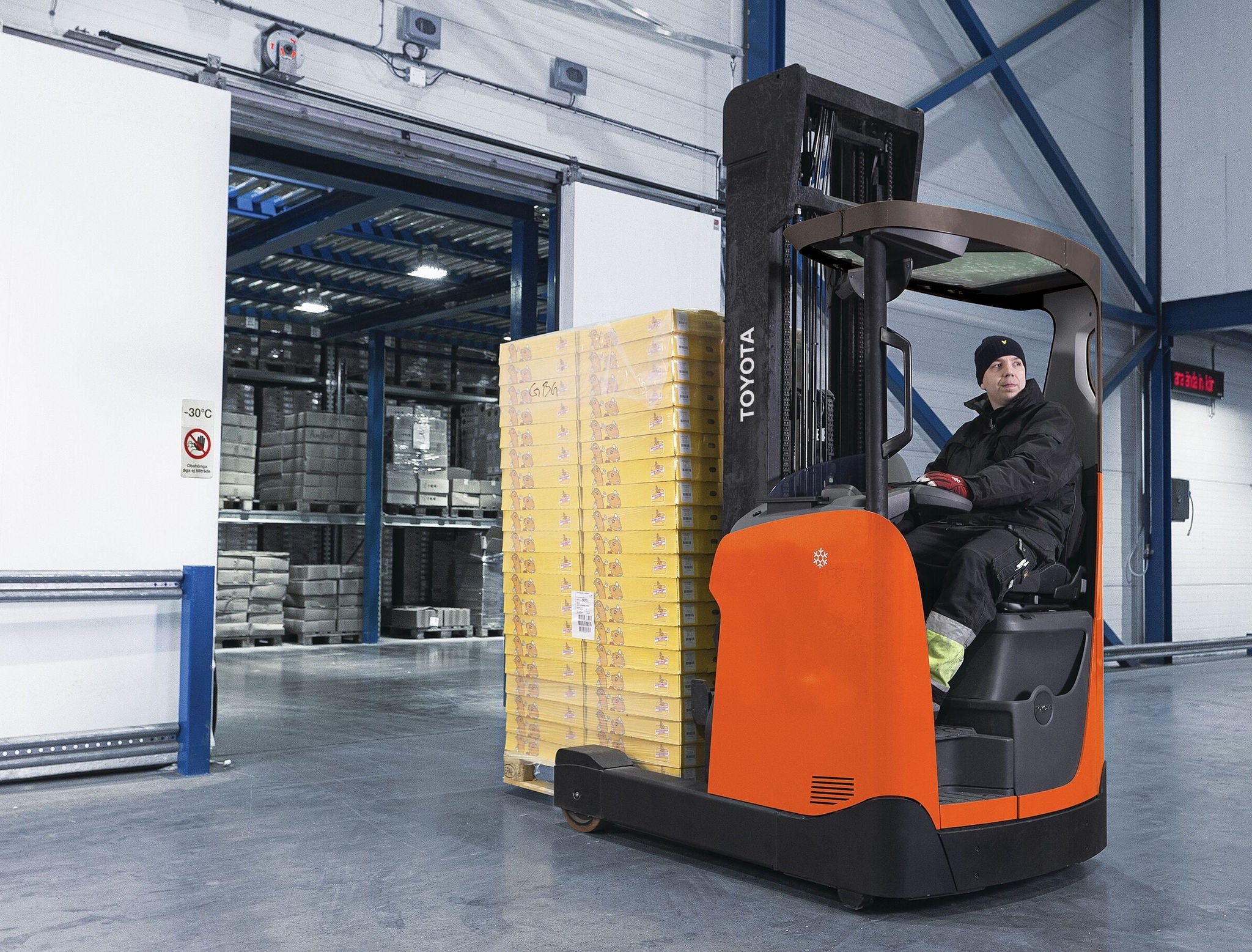 man with hat and heavy coat riding orange forklift in cold environment